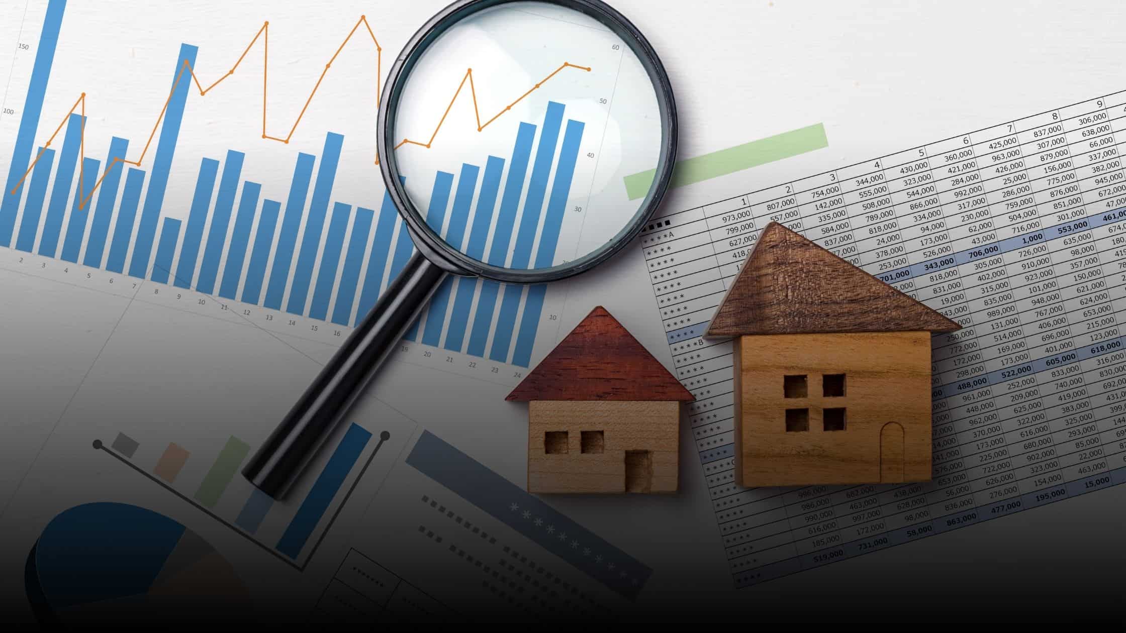  A magnifying glass highlighting real estate market graphs and charts, with two wooden house models in the foreground.